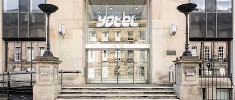 A hotel entrance with a glass facade, a sign reading 'yotel', and a number '68-73' above the entrance.