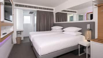 Una habitación de hotel moderna con una cama grande, mesitas de noche, un espejo y una televisión.
