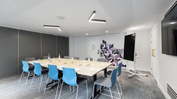 A conference room with a long table, blue chairs, a projector screen, and a geometric wall design.