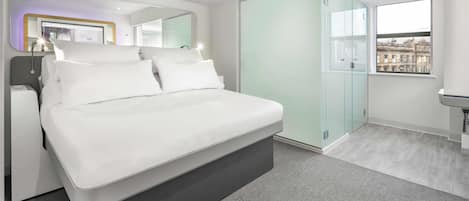 Un dormitorio moderno con una cama grande, un armario de vidrio y vistas a edificios a través de una ventana.
