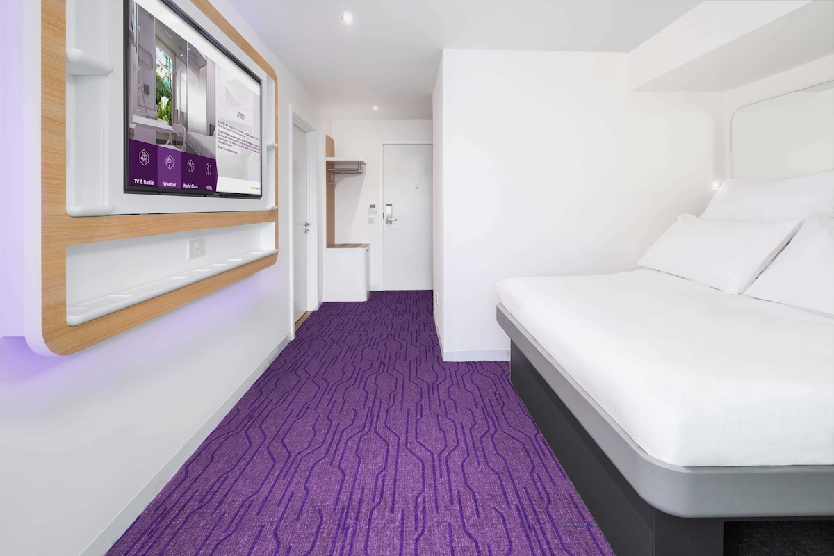 A modern hotel room with a large bed, a mounted TV, and a purple carpet.
