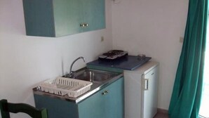 A compact kitchen with teal cabinets, a sink, a small refrigerator, and a window with a curtain. - Katerina Studios (Kefalonia)