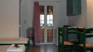 A room with two beds, a chair, a table, and a window with a curtain. - Katerina Studios (Kefalonia)