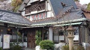Un edificio japonés tradicional con techo de tejas, vigas de madera y un farol de piedra.