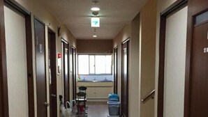 A long, narrow hallway with wooden doors on both sides, a window at the end, and a trash bin in the center. - Yamate Rest House - Hostel, Caters to Men (Tokyo)