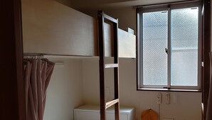 A dormitory room with bunk beds, a window, an air conditioning unit, and a power outlet. - Yamate Rest House - Hostel, Caters to Men (Tokyo)