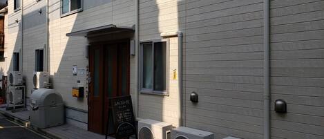A building with a wooden door, air conditioning units, and a signboard.