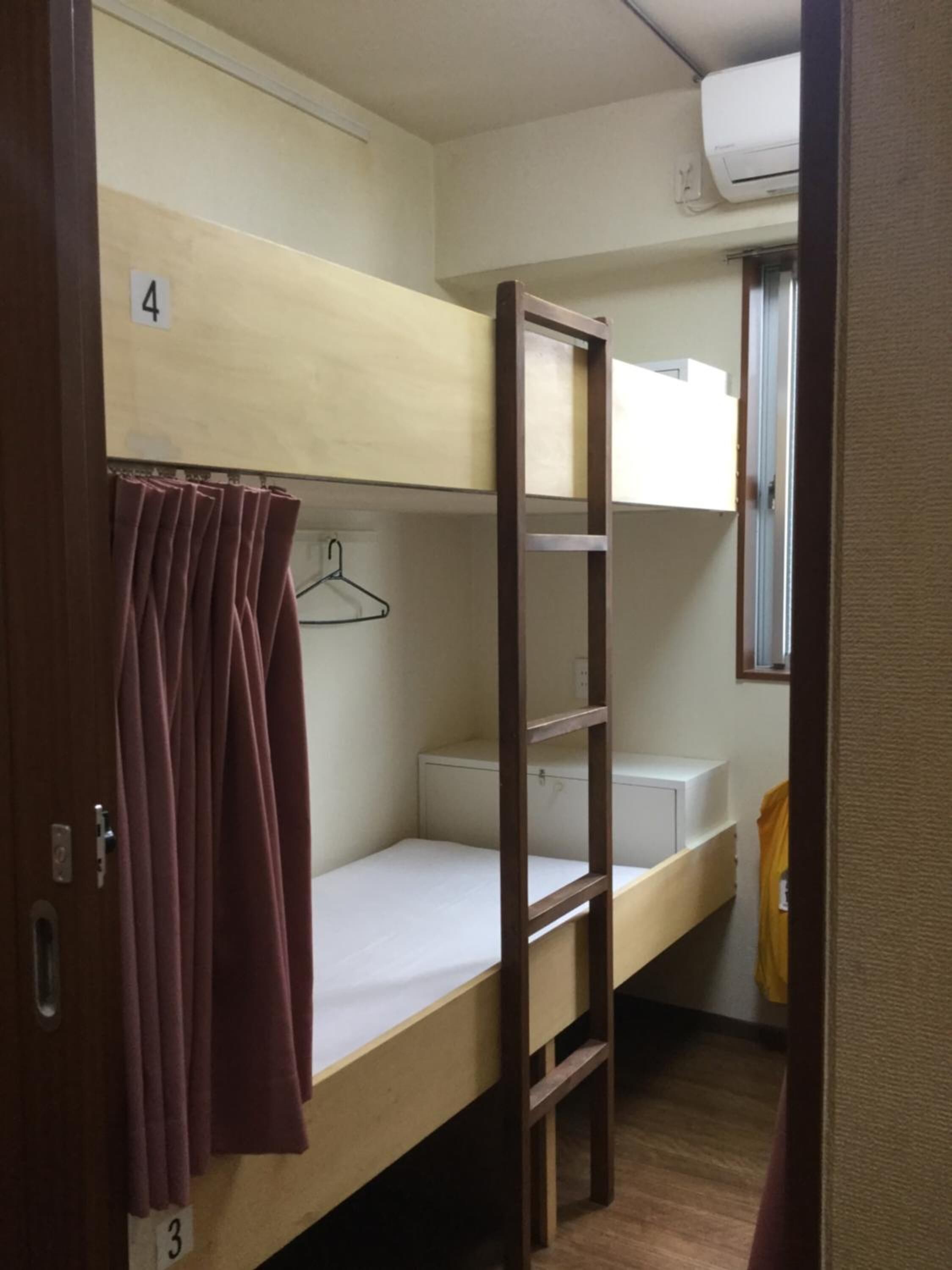 A bunk bed room with a wooden ladder, a white mattress, and a hanging garment.