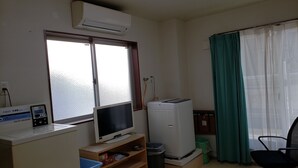 A small, well-lit room with a window, a washing machine, a television, and a desk with a computer. - Yamate Rest House - Hostel, Caters to Men (Tokyo)