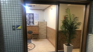 A hotel entrance with a reception desk, a small table, a potted plant, and a doormat with the hotel's name. - Nishikawaguchi Station Hotel Stay Lounge (Kawaguchi)