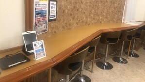A bar area with a wooden counter, multiple stools, and a tablet on the counter. - Nishikawaguchi Station Hotel Stay Lounge (Kawaguchi)
