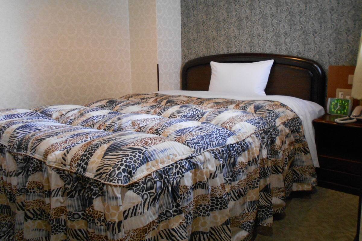 Una cama bien hecha con un edredón estampado, una almohada blanca y un cabecero de madera.