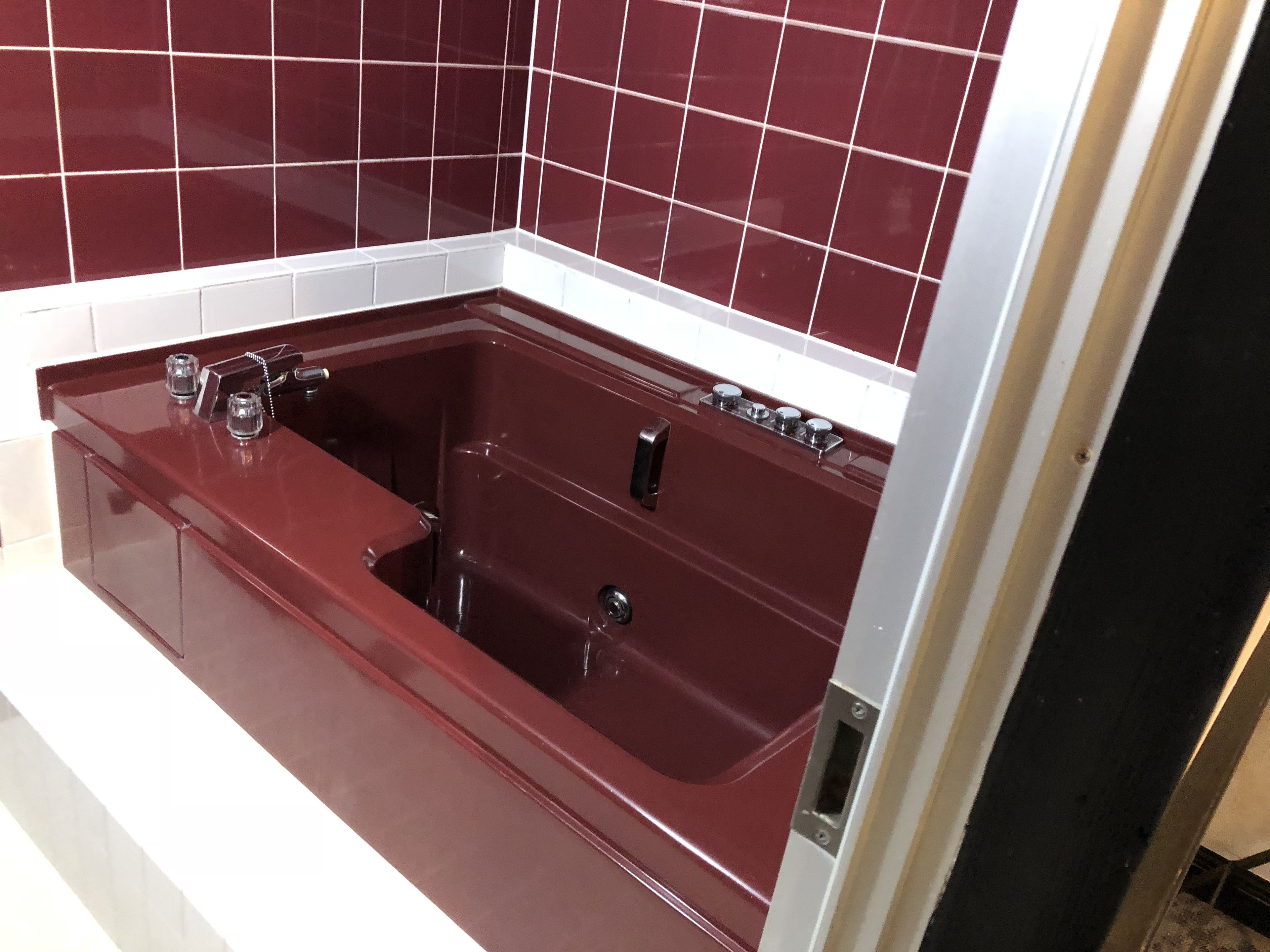 A modern bathroom with a large, deep red bathtub, white tiled walls, and a sleek, stainless steel faucet.