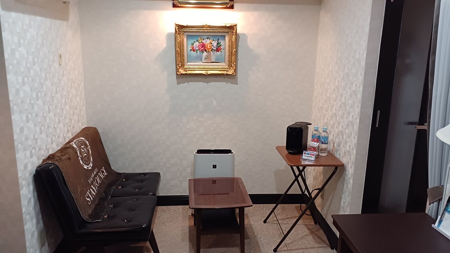 Una habitación con sofá, una mesita con un altavoz y botellas de agua, un cuadro en la pared y un purificador de aire compacto.