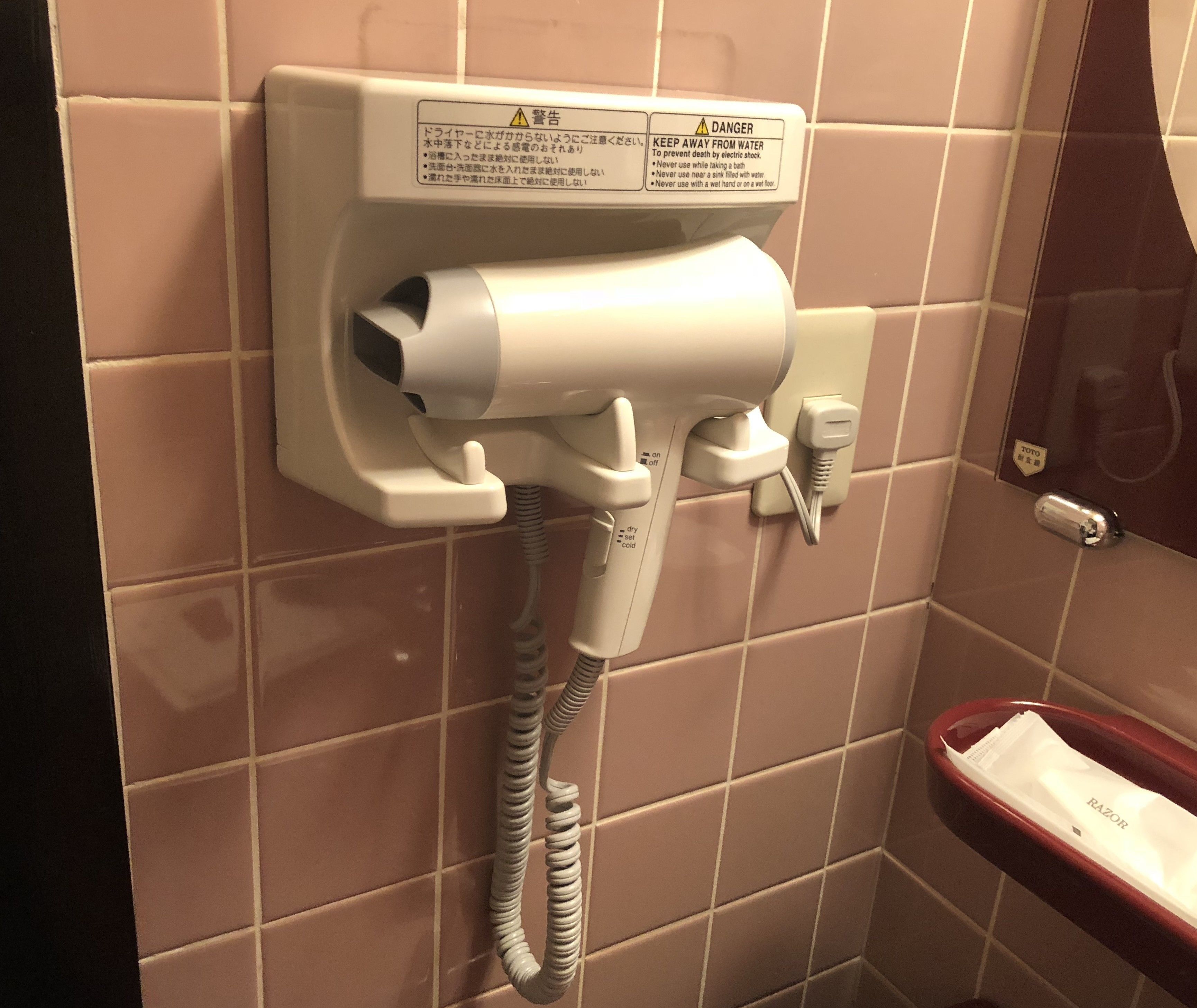 A hairdryer mounted on a wall with a warning label and a red basin.
