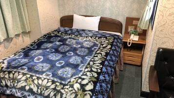 A neatly made bed with a patterned bedspread, a bedside table with a telephone, and a chair.