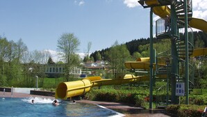 Ein Wasserpark mit einer großen, gelben Wasserrutsche, einem Schwimmbecken und einem Rettungsturm.