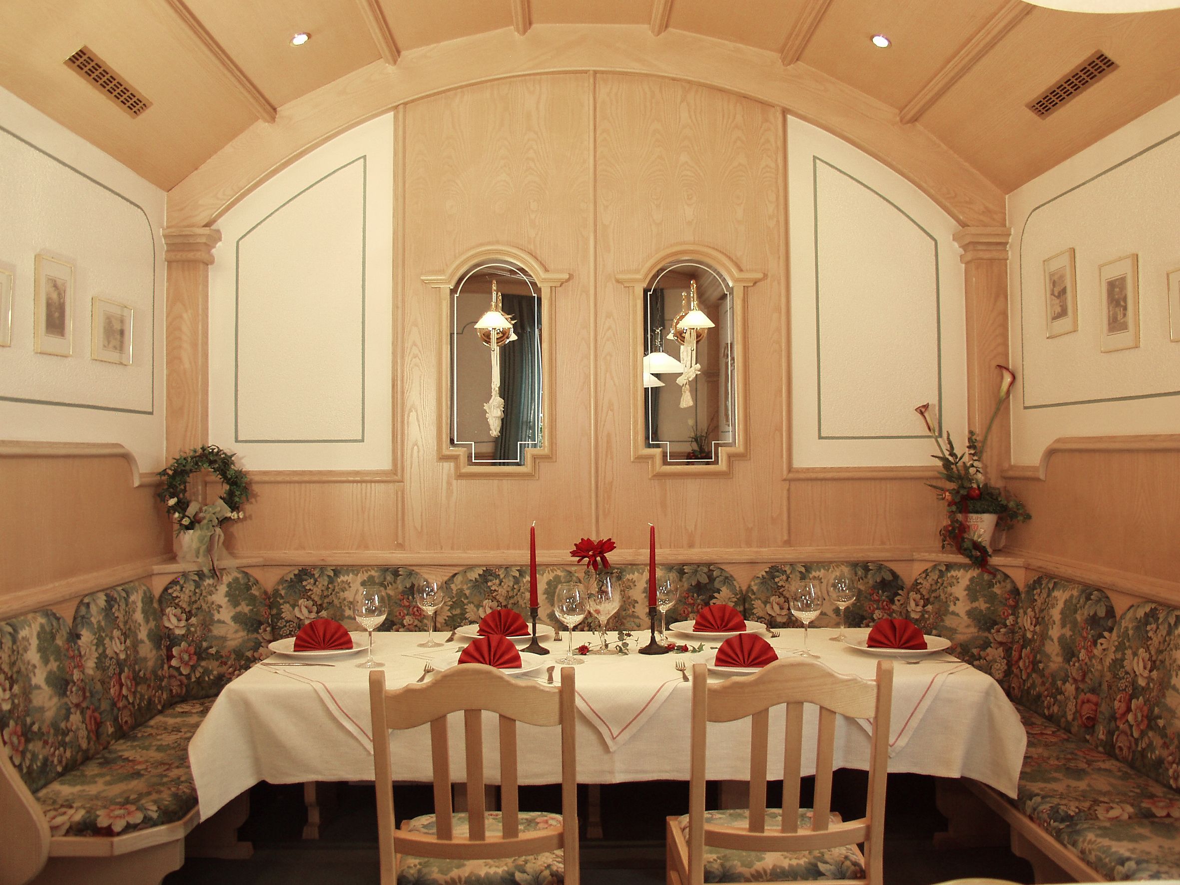 Une salle à manger élégante, avec une longue table, des motifs floraux sur les sièges et deux lustres fixés au mur.