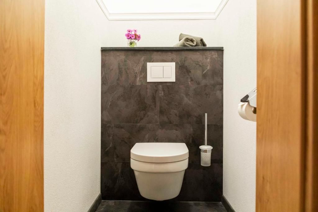 A compact bathroom with a toilet, a wall-mounted flush handle, and a small trash bin.