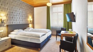 Ein Hotelzimmer mit Bett, Nachttischen, Schreibtisch mit Stuhl, Fernseher und einem Fenster mit Vorhängen.