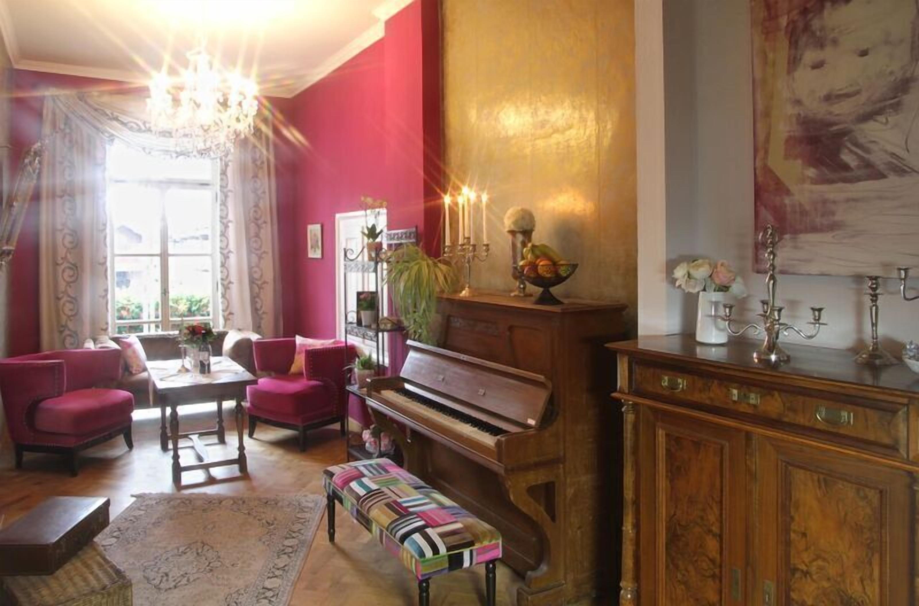A living room with a grand piano, red walls, and a chandelier.
