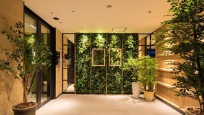 A modern hotel lobby with a green wall, potted plants, and a wooden reception desk. - Super Hotel Sakai Marittima (Sakai)