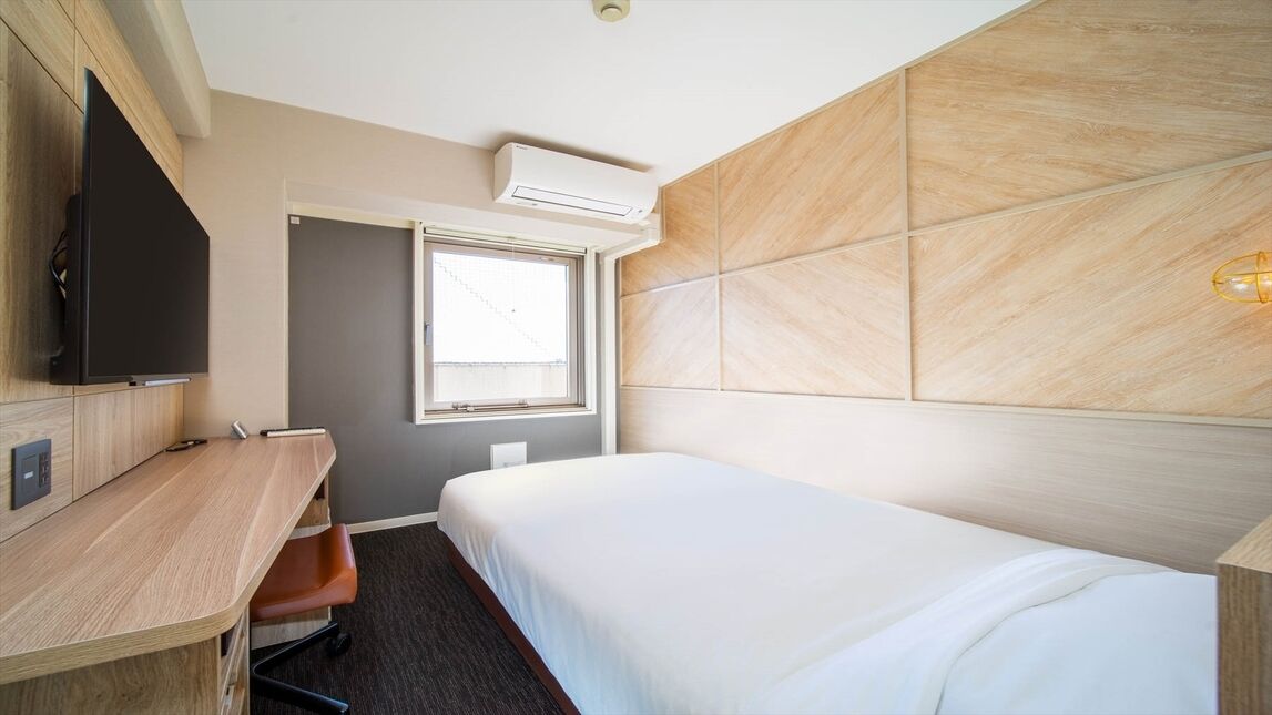 A hotel room with a bed, a desk, a chair, a television, and a window.