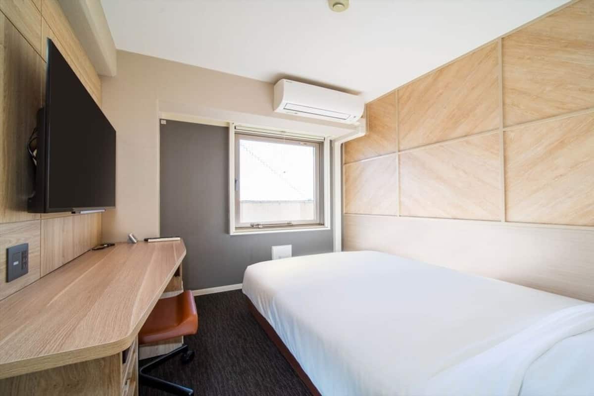 A hotel room with a bed, a desk, a chair, a television, and a window.