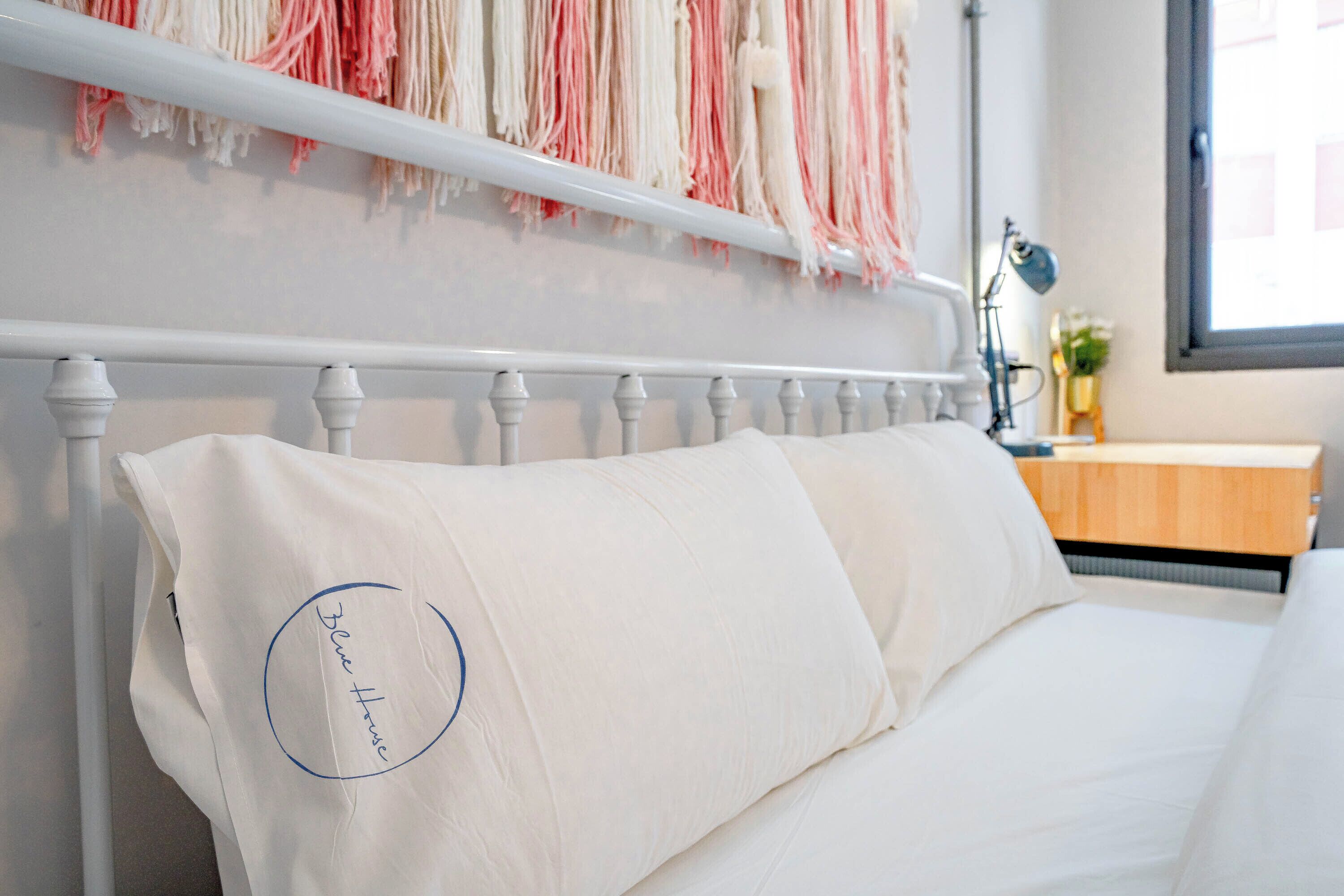 Una cama bien hecha con ropa de cama y almohadas blancas, un cabecero blanco y una mesita de noche con una lámpara.