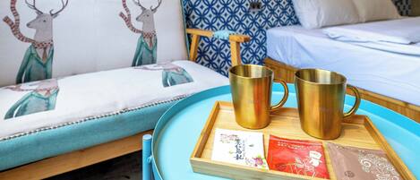 Habitación de hotel con cama, sofá con cabecera estampada y bandeja con dos tazas doradas y una tarjeta.