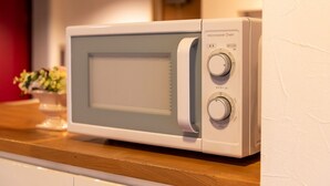 A microwave oven with two control knobs and a digital display, placed on a wooden countertop. - Niiza Daily Hotel (Niiza)