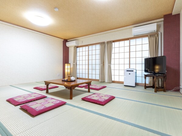 A traditional Japanese room with tatami flooring, a low table with a tea set, a television on a stand, and a sliding door with curtains.