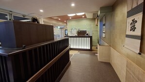 A reception area with a wooden reception desk, a counter with a digital display, and a wall with a framed artwork. - Business Ryokan Akashiya Annex (Akashi)