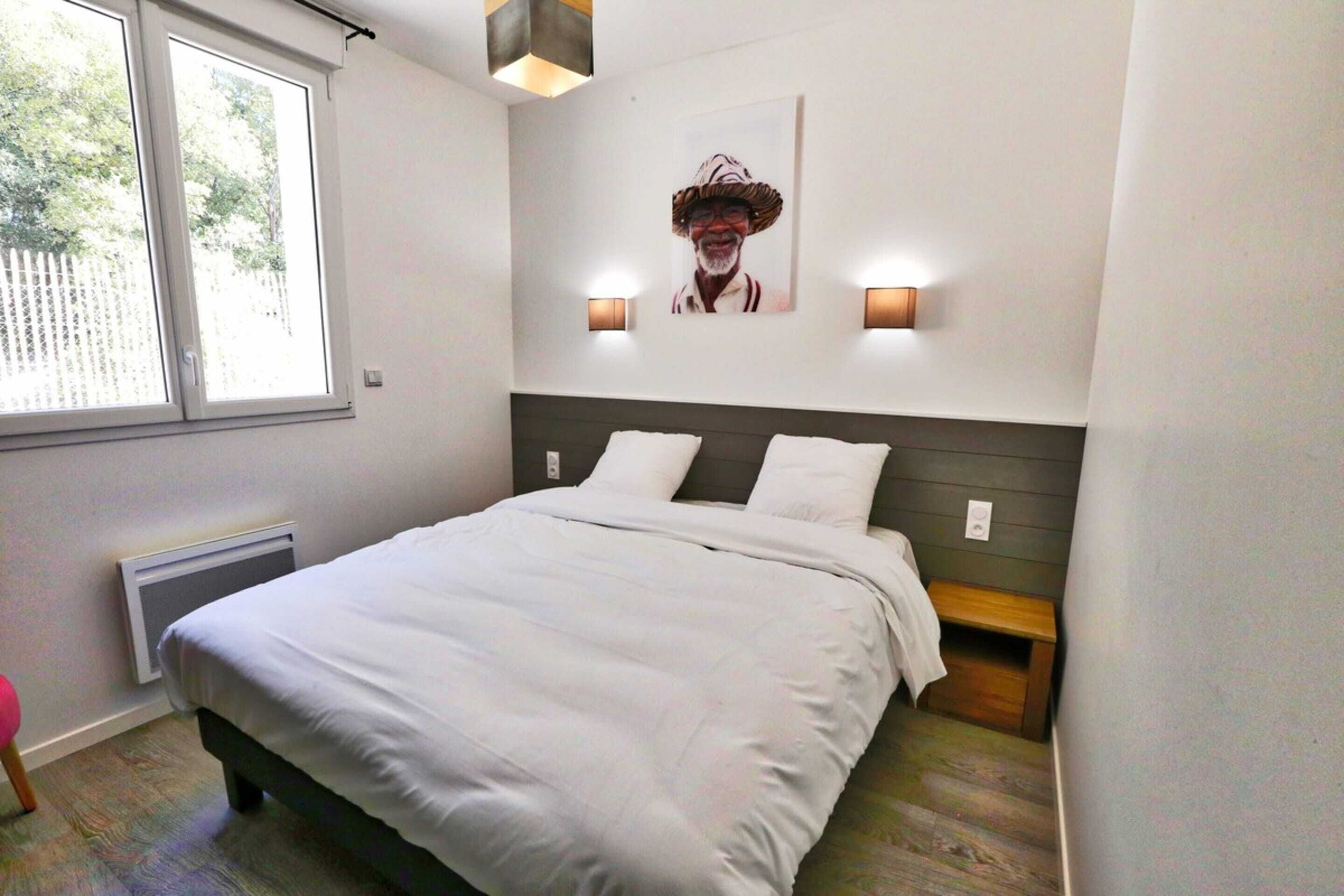 Ein Schlafzimmer mit Bett, Kopfteil, zwei Wandleuchten, einer Heizung und einem Fenster.