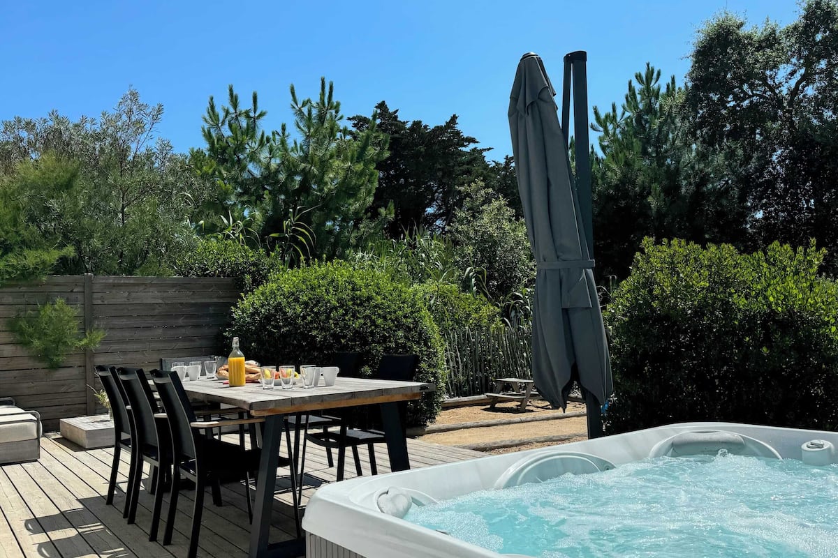 A patio with a table and chairs, a hot tub, and a wooden fence.