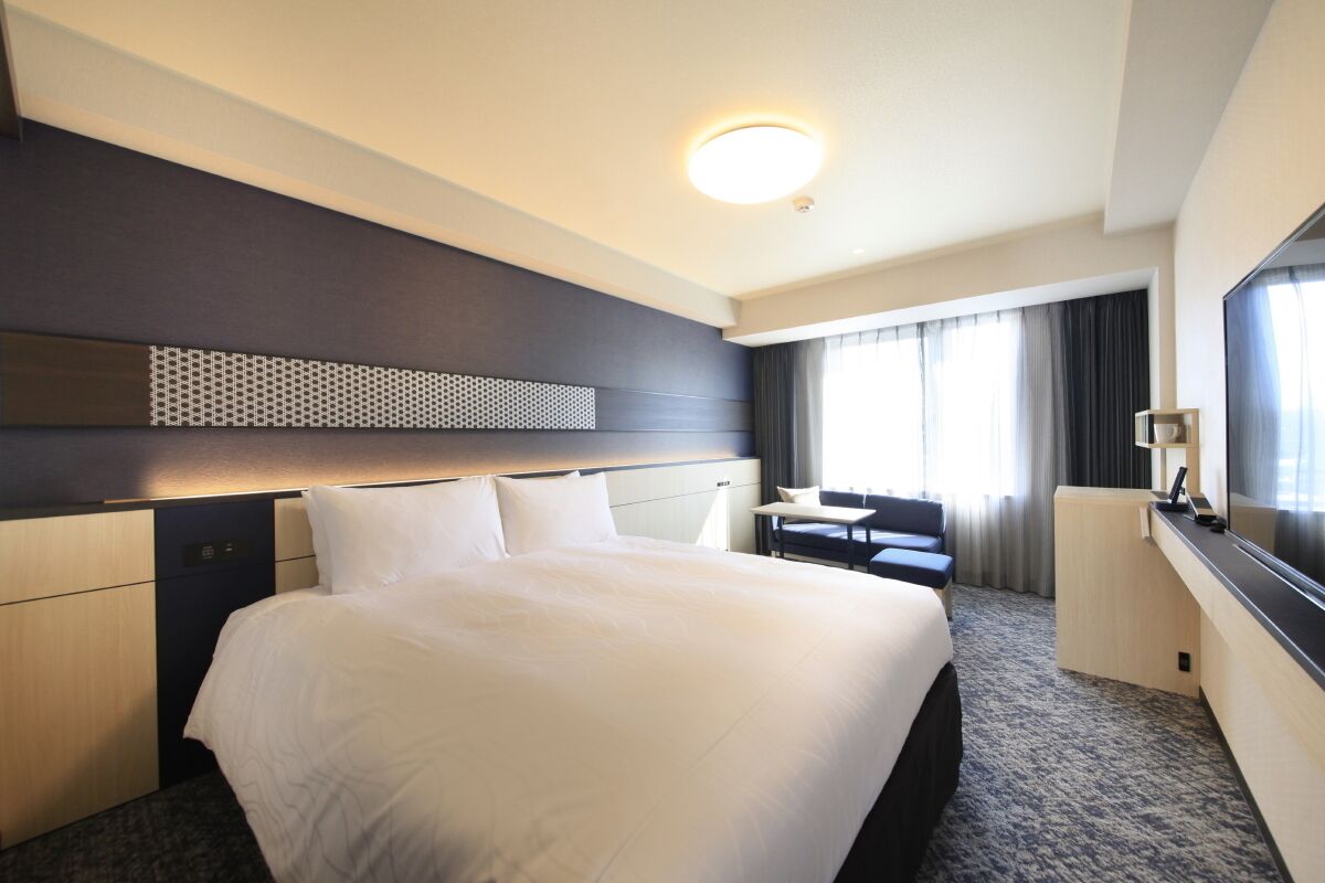 Una habitación de hotel con una cama grande, un escritorio, una silla, un televisor y una ventana con cortinas.