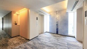 Un pasillo moderno de hotel con piso alfombrado, un panel de luz vertical y un ventanal que proporciona luz natural.