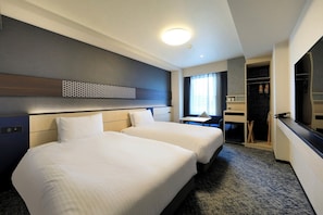 Ein Hotelzimmer mit zwei Betten, einem Schreibtisch, einem Kleiderschrank und einem Badezimmer.