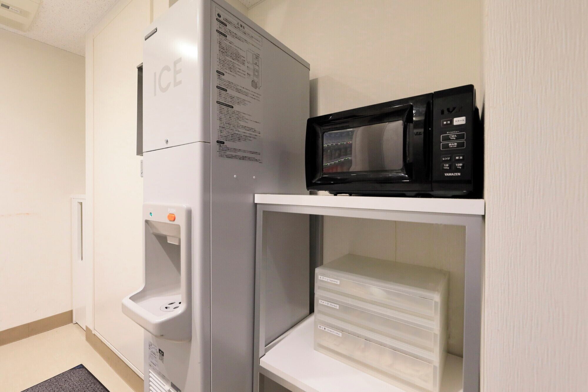 Una cocina con refrigerador, microondas y un pequeño estante con cajones.