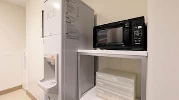 Una cocina con refrigerador, microondas y un pequeño estante con cajones.