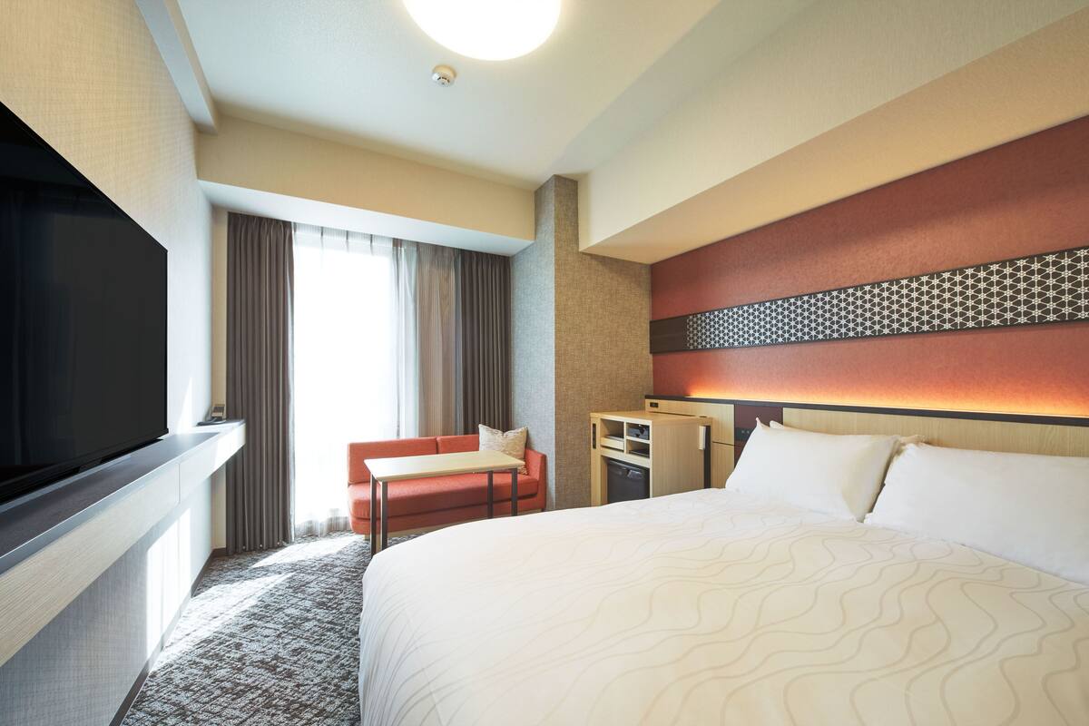 Habitació d'hotel amb un llit gran, una televisió, un escriptori i un sofà.
