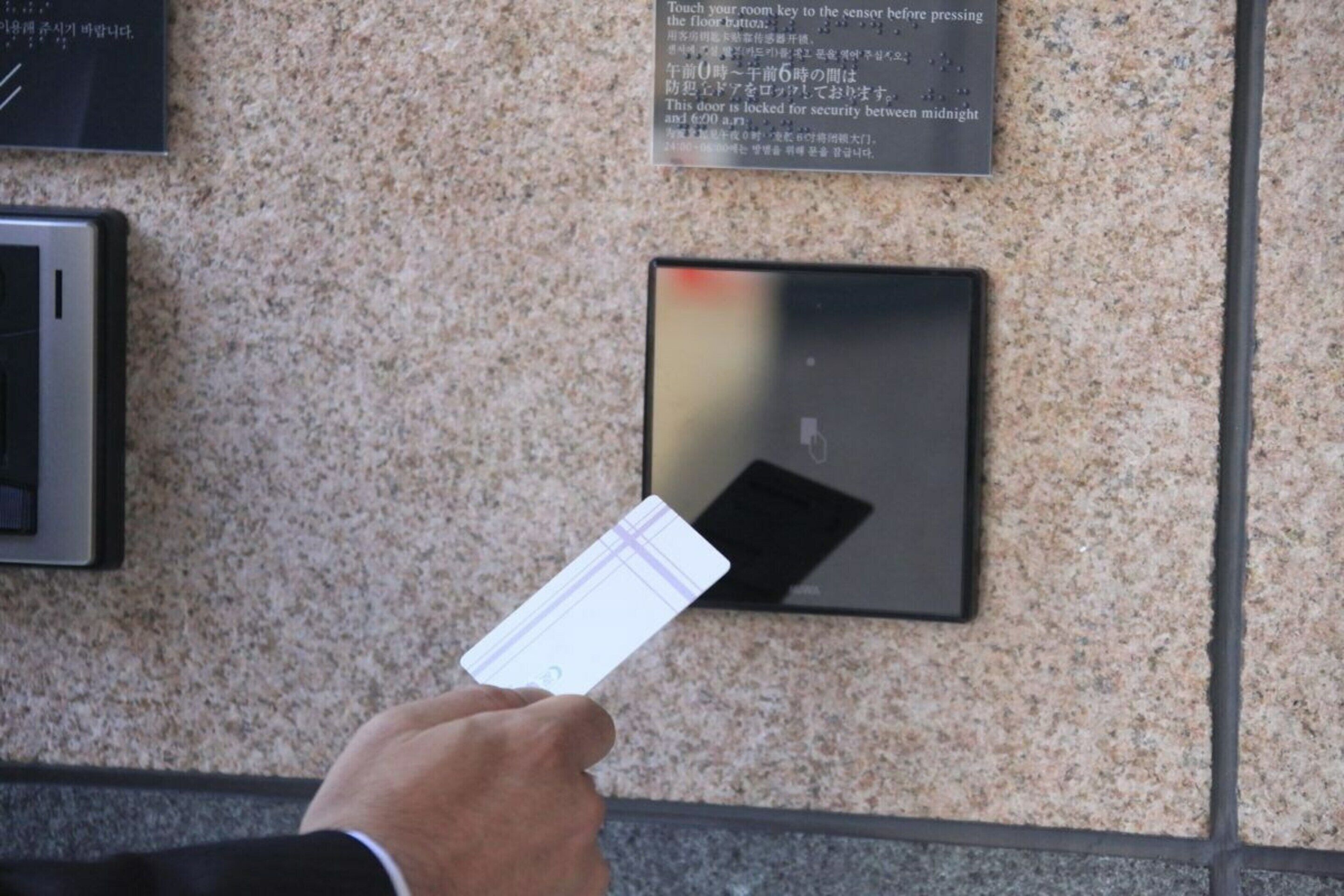 A hand holding a card near a sensor on a wall, with a security sign above it.