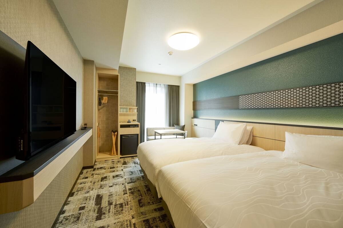 Habitació d'hotel amb televisió de pantalla plana, dos llits, escriptori i armari encastat.