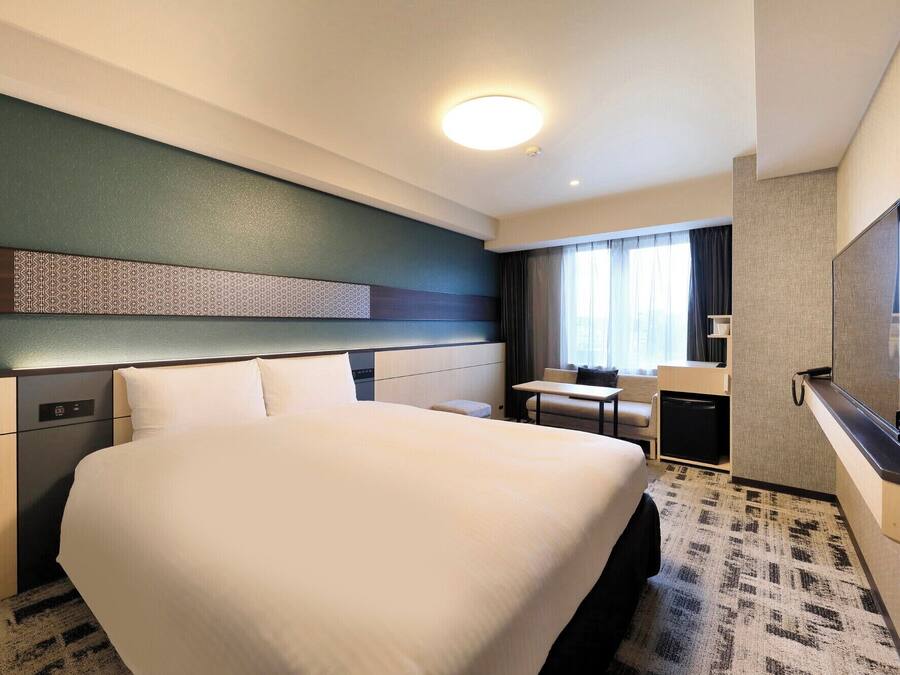 A hotel room with a large bed, a desk, a television, and a window with curtains.