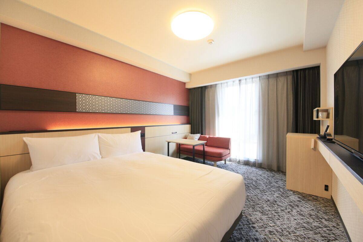 Una habitació d'hotel amb un llit gran, una taula de treball, una cadira, un televisor i una finestra amb cortines.