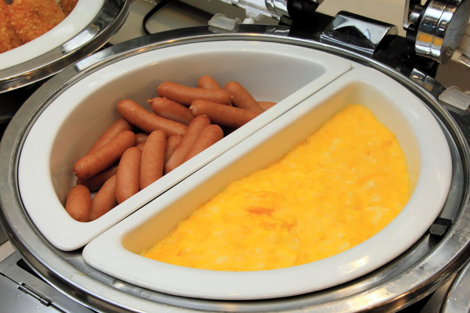 A buffet with two sections; one with hot dogs and the other with a yellow omelette.