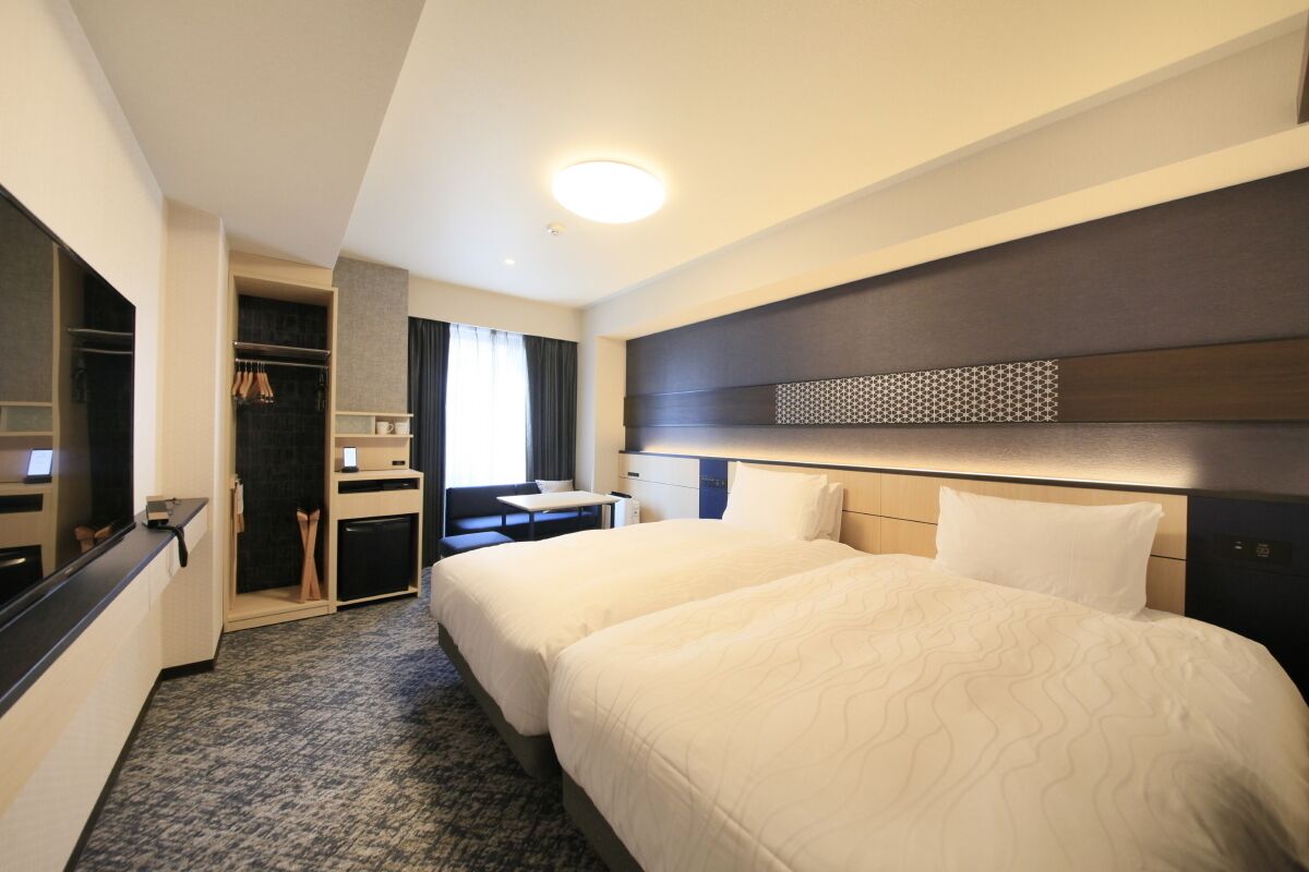 Habitación de hotel con dos camas, un escritorio, un armario y un espejo.