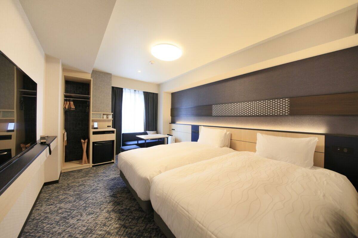 Habitació d'hotel amb dos llits, una taula de treball, un armari i un mirall.