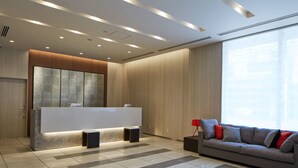 Un área de recepción moderna con un mostrador, un sofá y un amplio ventanal que proporciona luz natural.