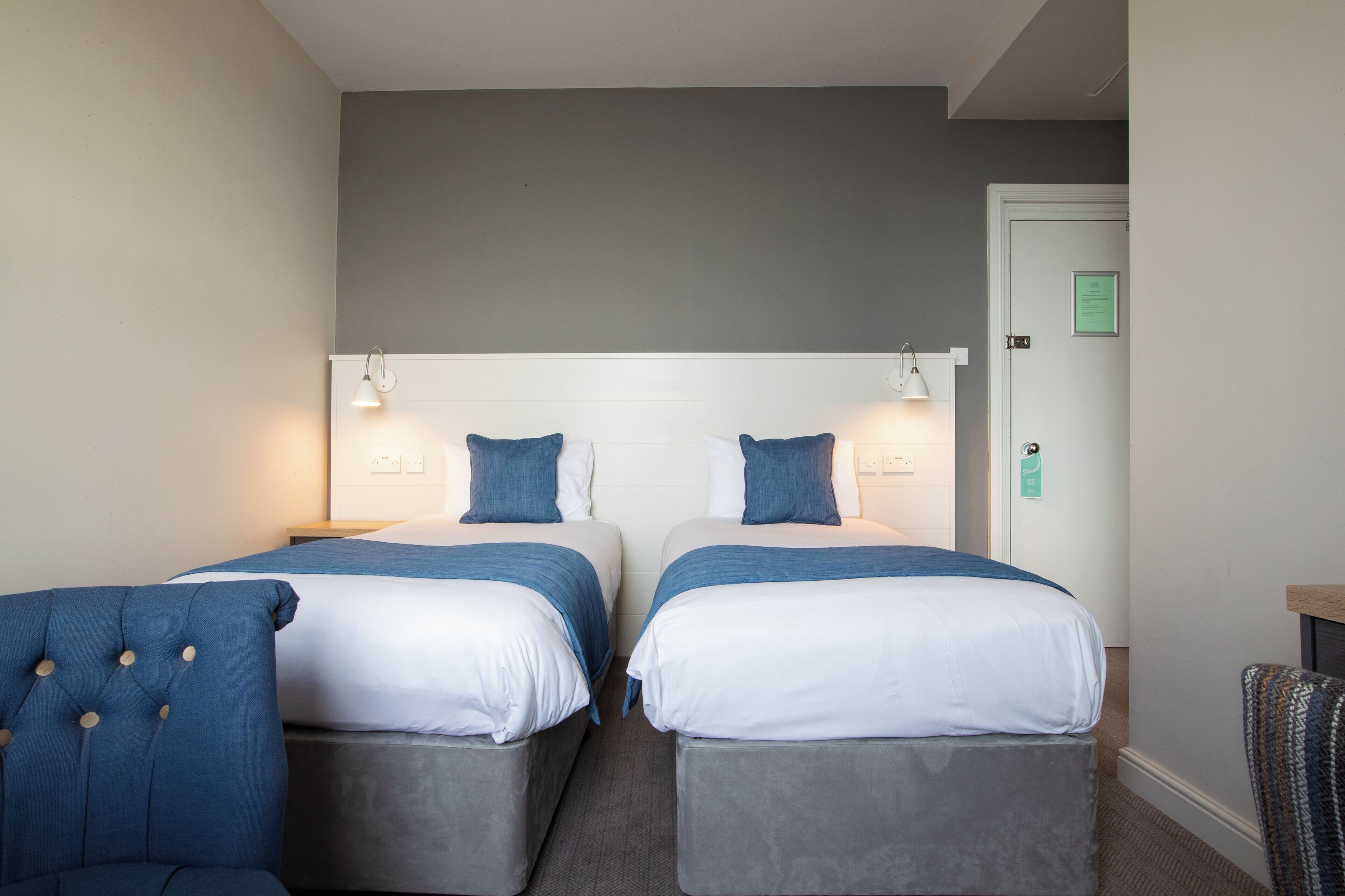 Een hotelkamer met twee bedden, grijze hoofdeinden en blauw beddengoed.